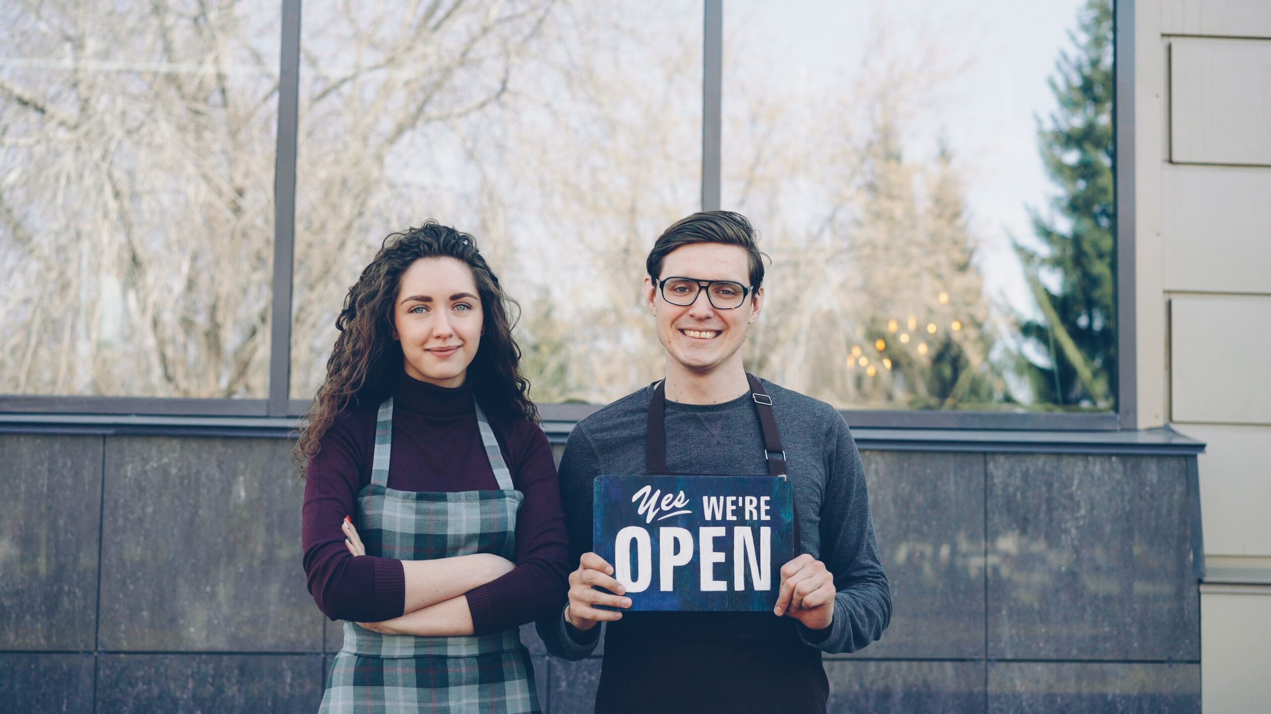 Small business owners holding up a sign that says "We're open"